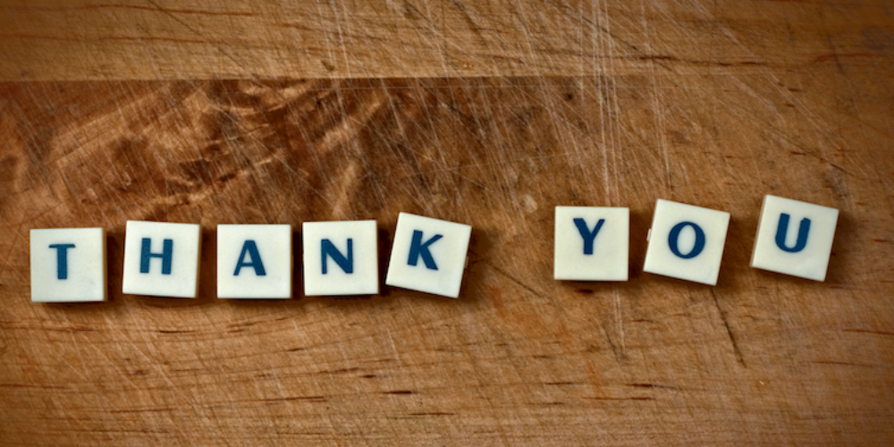 Scrabble tiles on a wooden table spelling out THANK YOU