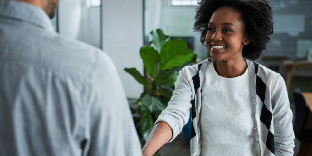 Smiling African American woman shaking hands with male in lobby