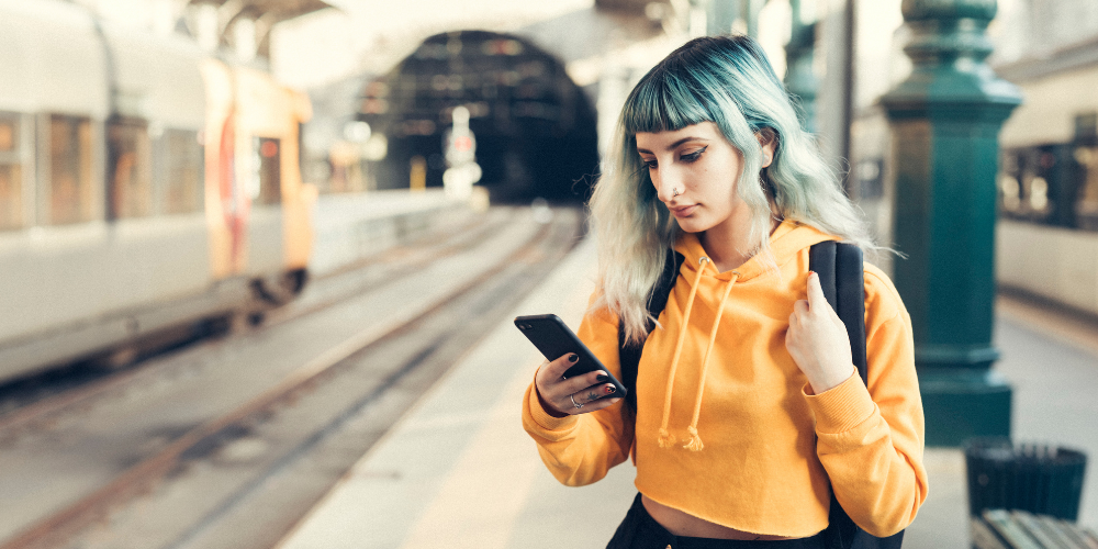 girl with green hair looking at phone in train station