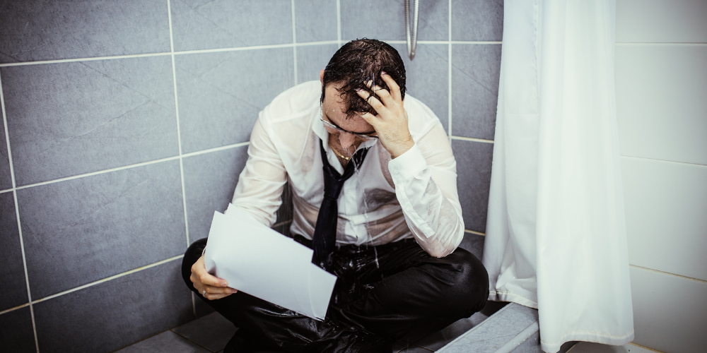devastated man sitting in shower clothed looking at papers