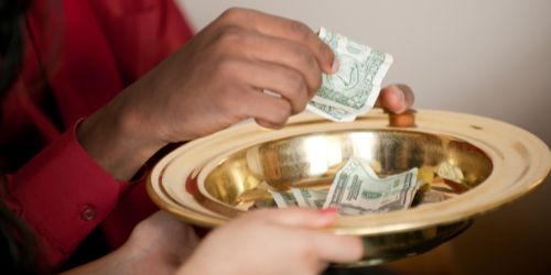 someone putting a dollar in a church offering plate
